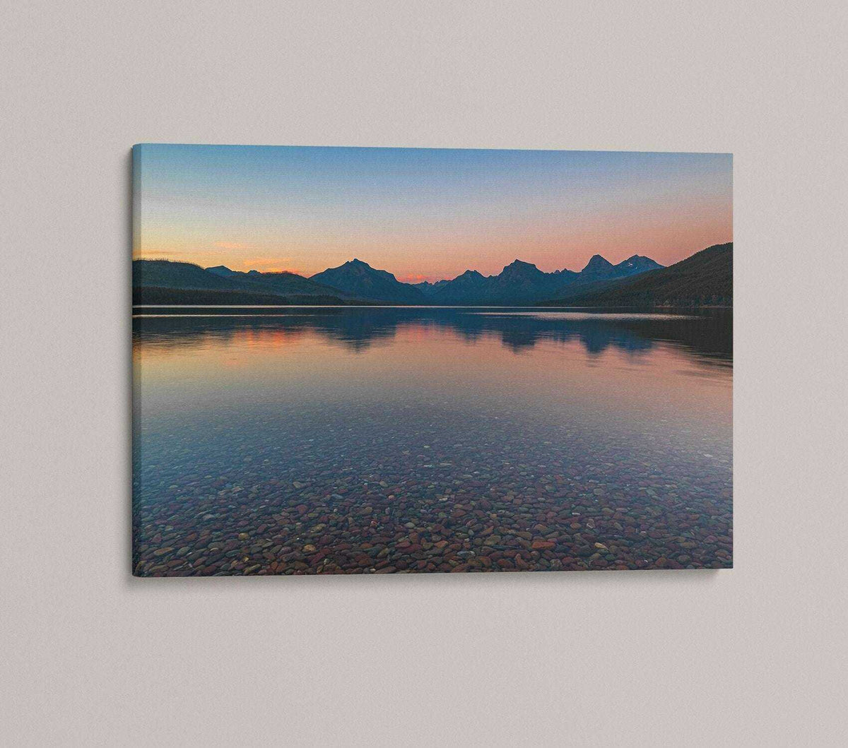 Glacier National Park Print showing a blue mountain lake at sunset, with a pink-orange sky and visible shoreline stones