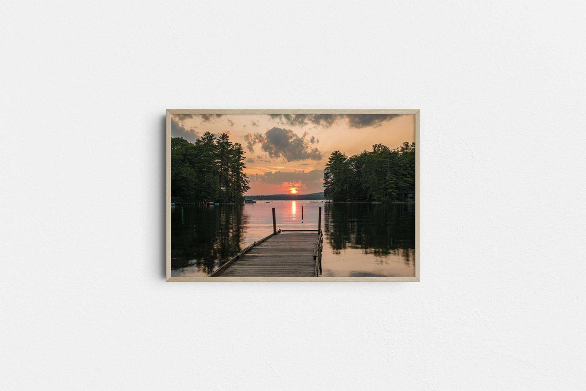 Great East Lake Dock Sunset Print showing a wooden dock on calm water beneath an orange sunset, framed in light wood