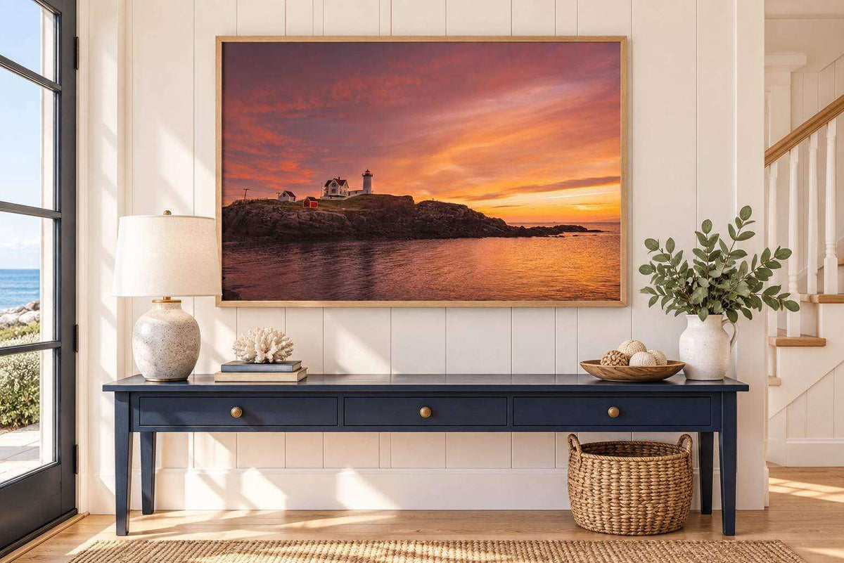 Nubble Lighthouse Wall Art featuring a rocky Maine coastline, calm water, and vivid orange-pink sunrise tones in a wood frame