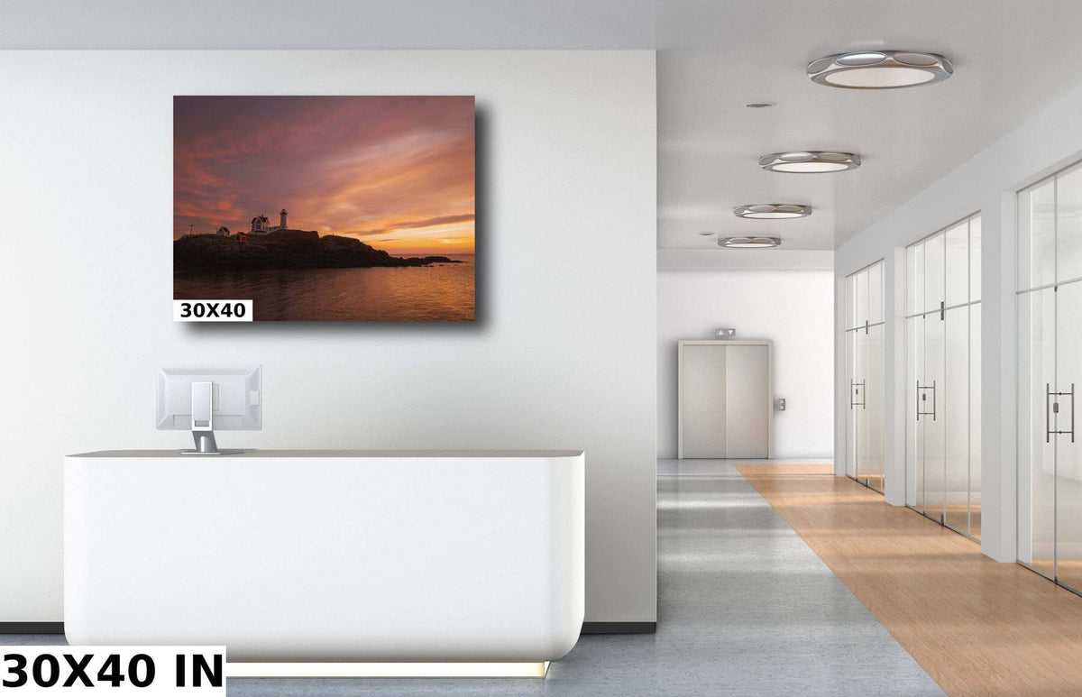 Nubble Lighthouse Wall Art with a dark coastal silhouette, rugged rocky shore, and warm orange-pink sunset over the water