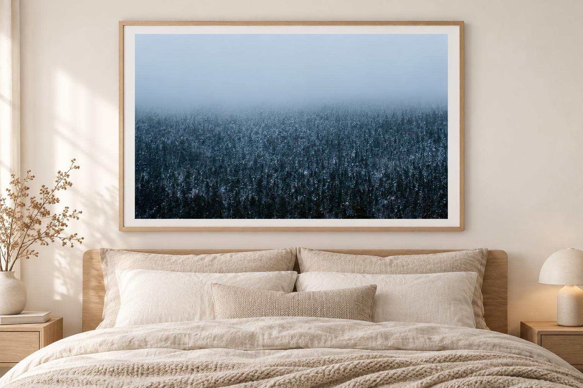 Winter Forest Wall Art print showing a dense snowy evergreen forest fading into blue-gray mountain fog, framed in natural wood